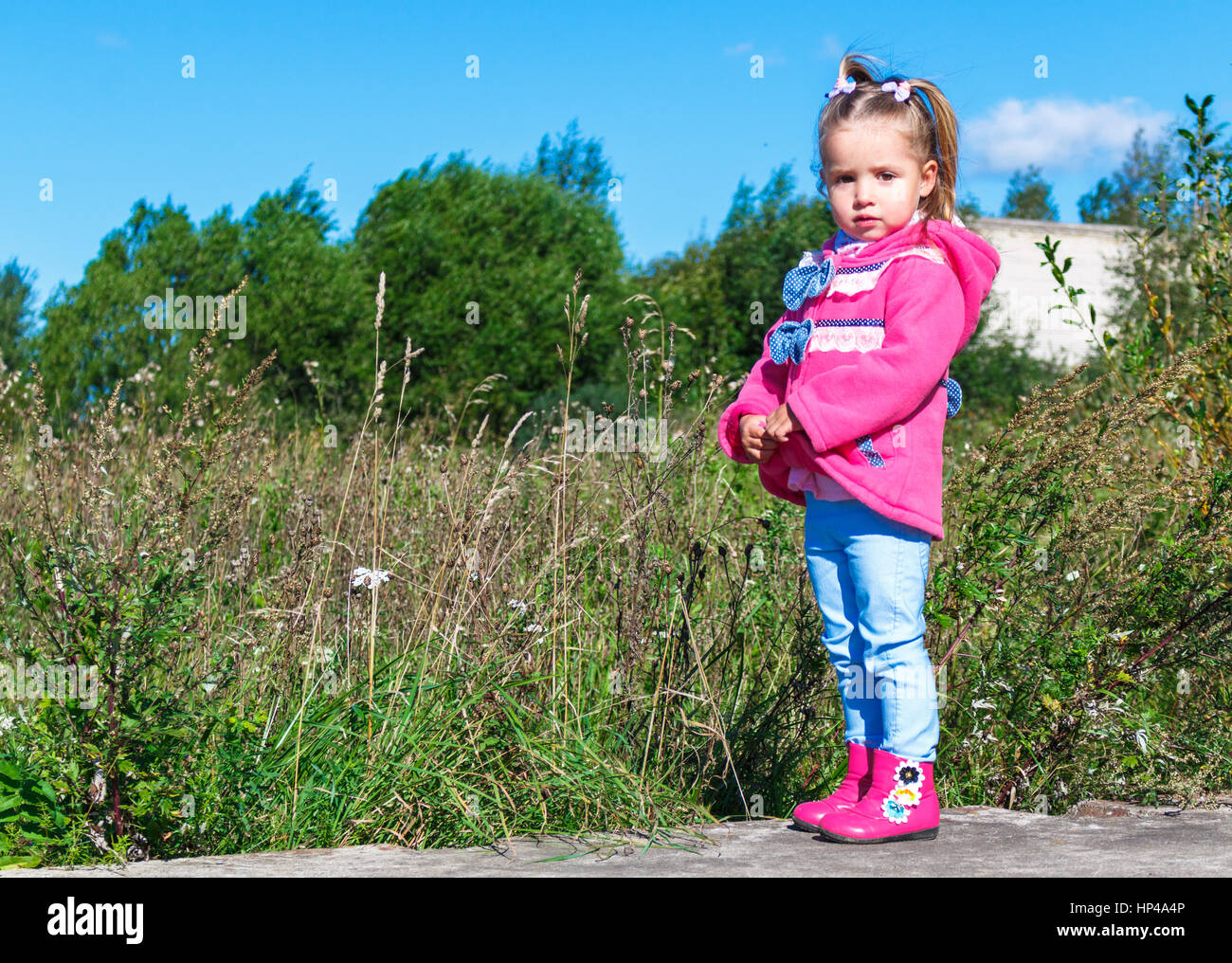 Little girl in a pink coat, jeans and pink boots walking in the park ...
