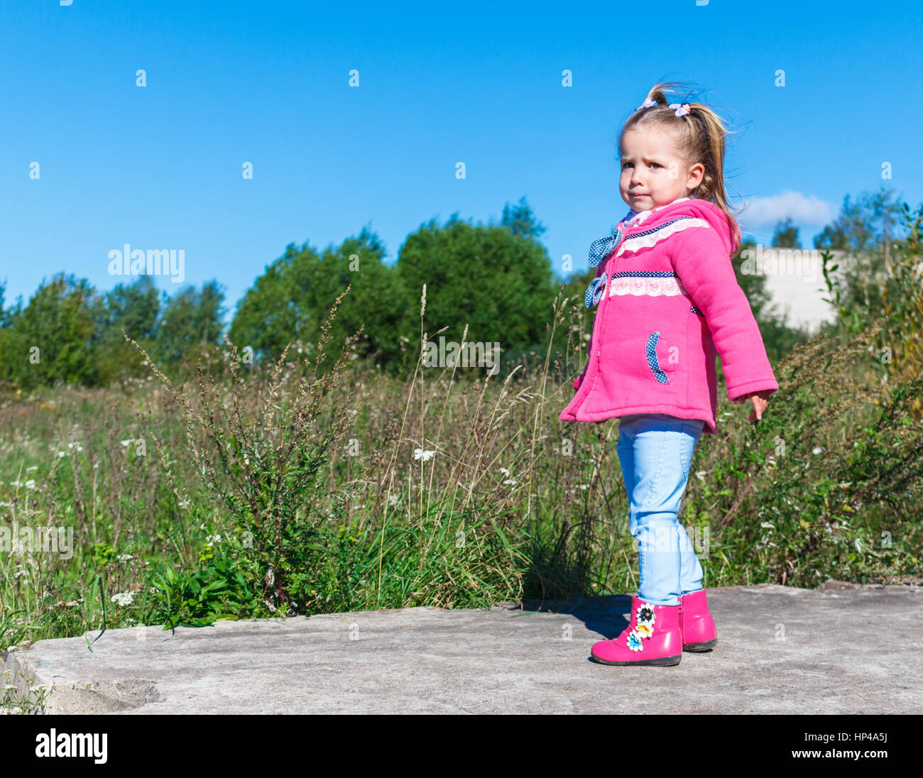 Little girl in a pink coat, jeans and pink boots walking in the park ...