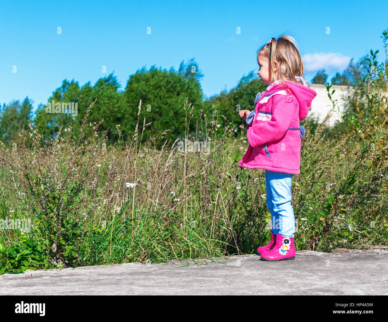 Little girl in a pink coat, jeans and pink boots walking in the park ...