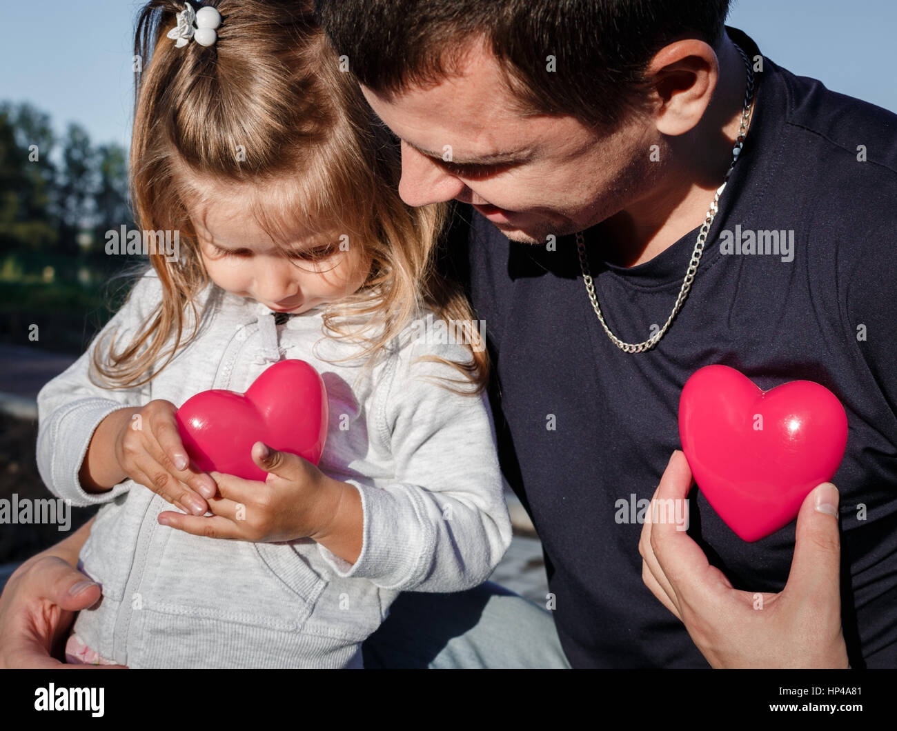 man and baby holding a two red plastic heart. father hugs the daughter ...