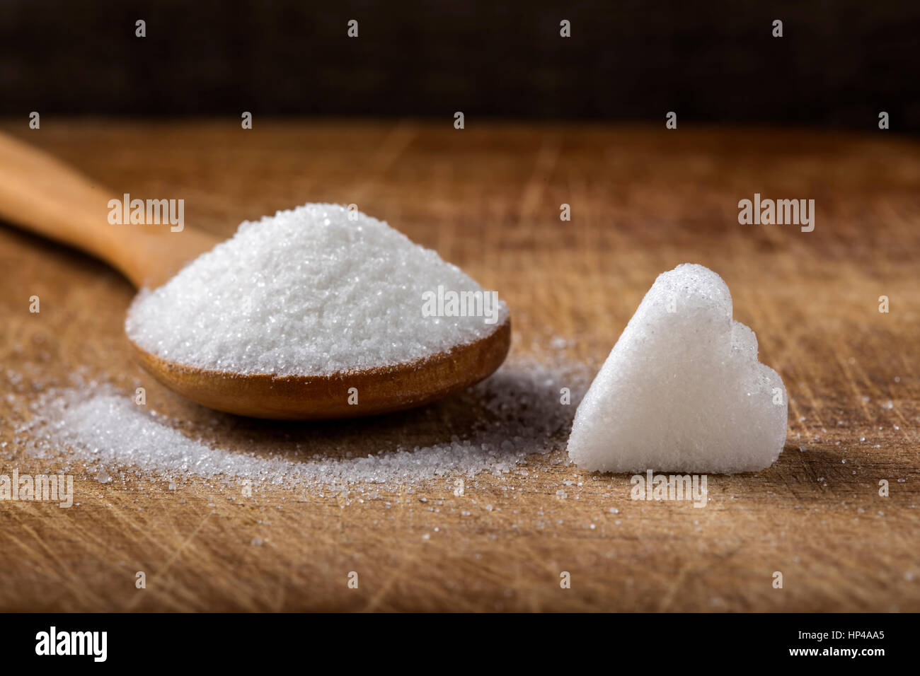 One sugar cube in heart shape and wooden spoon filled with sugar on
