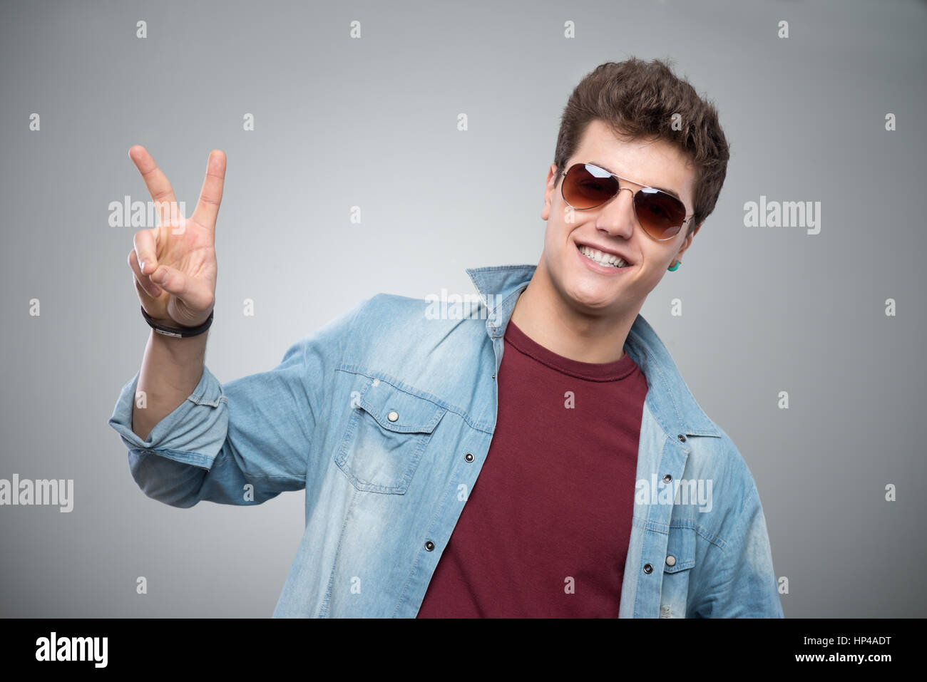 Cheerful cool guy in sunglasses making V sign on gray background Stock Photo