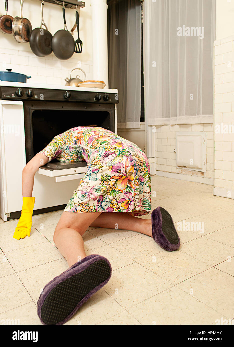 A woman laying on a kitchen floor with her head in an oven. Stock Photo