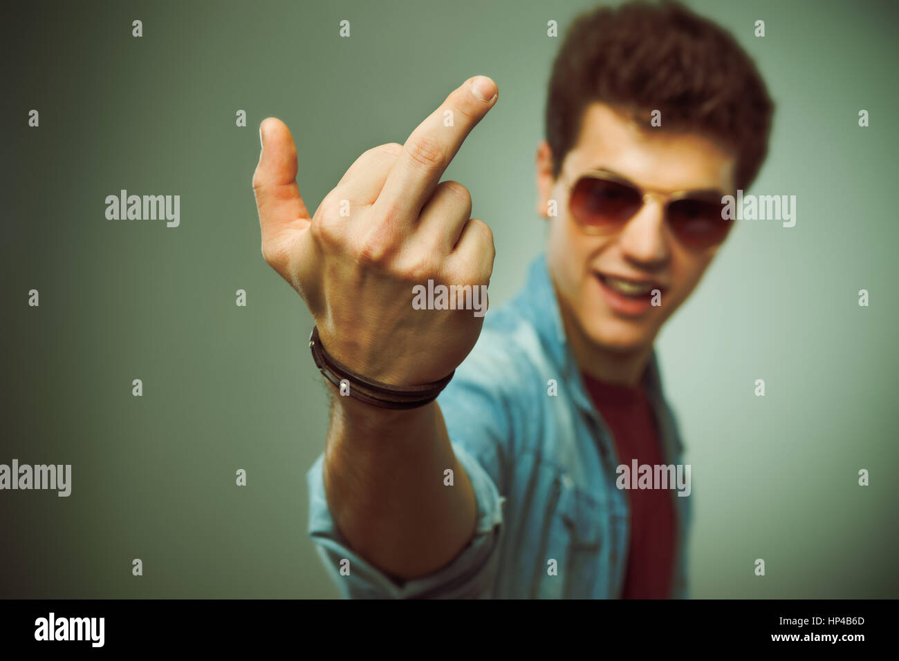 Confident smiling teenager in sunglasses showing middle finger Stock Photo