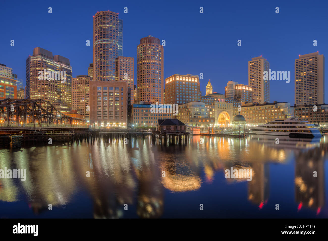 The skyline reflects off the still waters of the harbor in the last hour before sunrise as a new day begins in Boston, Massachusetts. Stock Photo