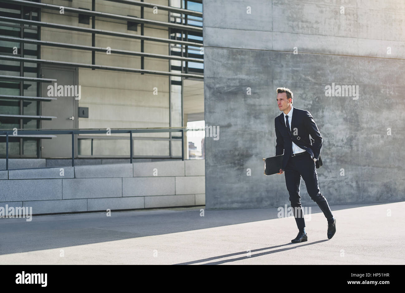 Young male in formal dark suit with skateboard at hand walking in hurry  down bright street Stock Photo - Alamy