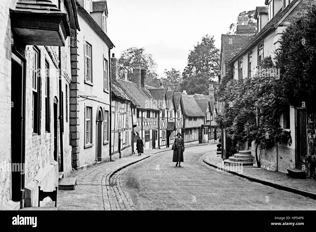A lady walking in the middle of a quite Warwick road carrying a bag. In the distance another lady is walking on the pavement, sidewalk, away from the camera. Photograph taken in the 1940's, restored from a high resolution scan taken from the original negative. Stock Photo