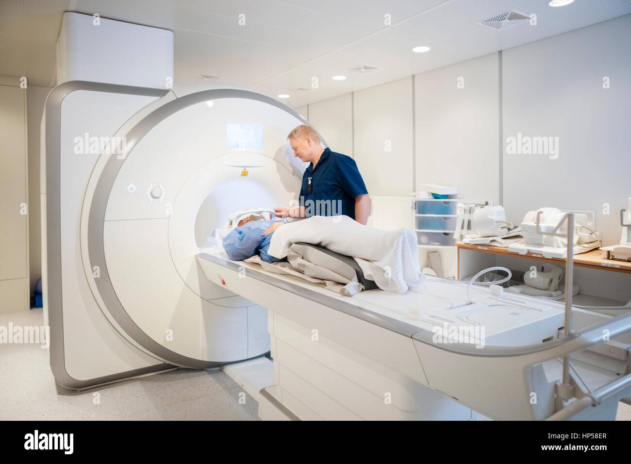 Doctor Putting Coil On Female Patient's Head Undergoing MRI Scan Stock