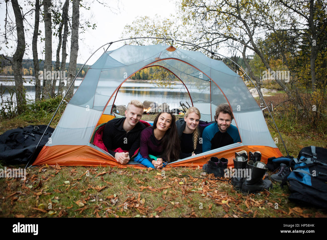 Smiling Young Friends Lying In Tent On Lakeshore Stock Photo