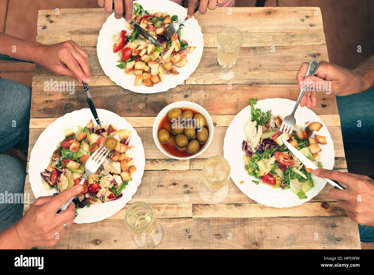 Friends having informal dinner together. Salad, olives, champagne on wooden table. View from