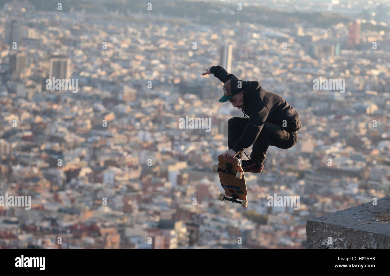 A boy jumps on his longboard on a nearby hill to the city of barcelona Stock Photo