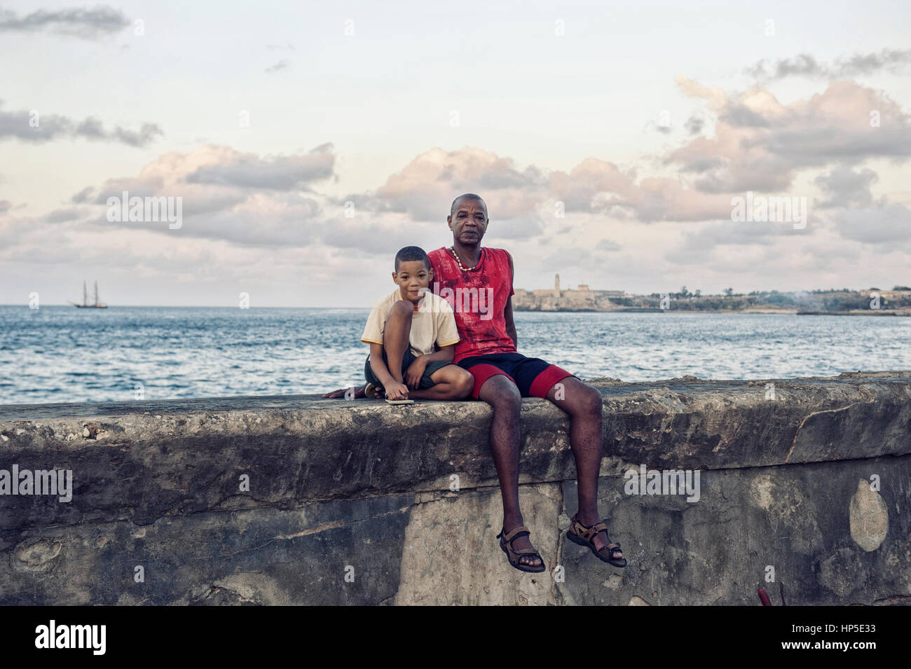 padre e figlio seduti sul muretto del Malecon in posa per una foto insieme. Stock Photo