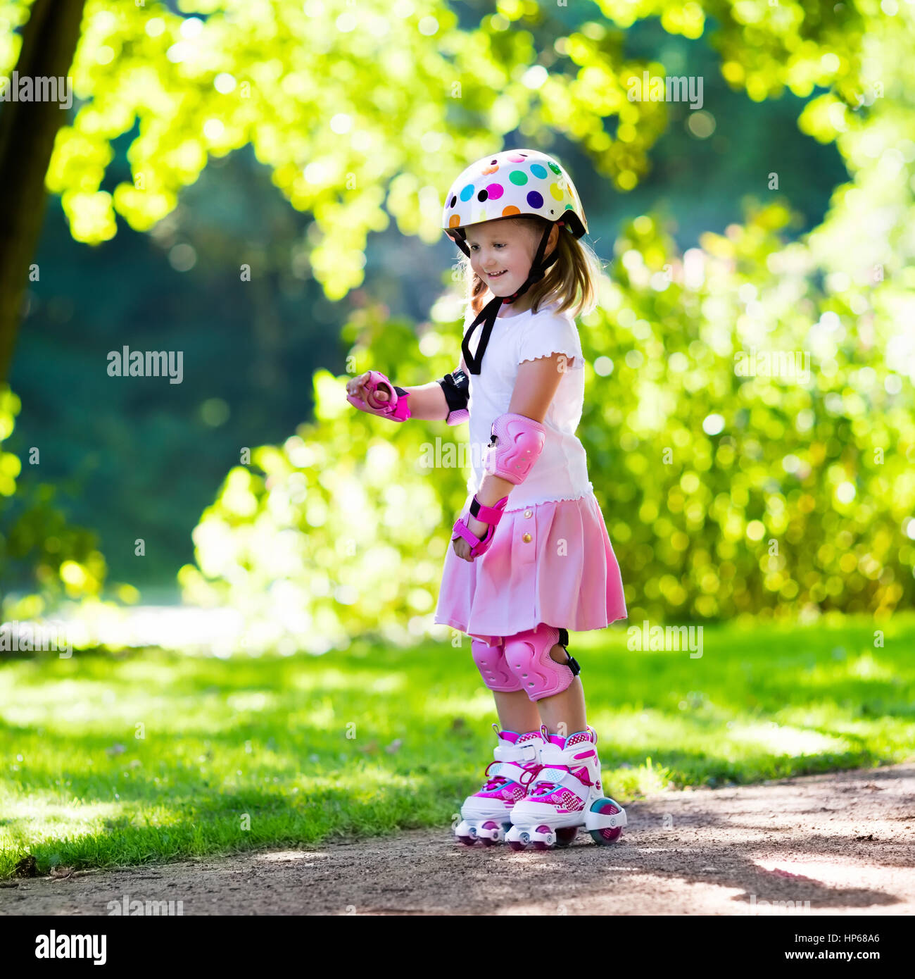 Little girl learning to roller skate in sunny summer park. Child