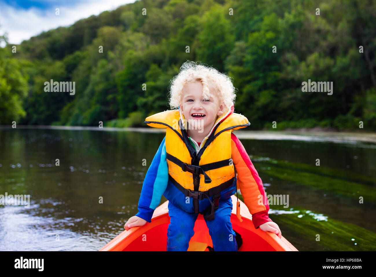 Happy kid enjoying kayak ride on beautiful river. Little curly toddler