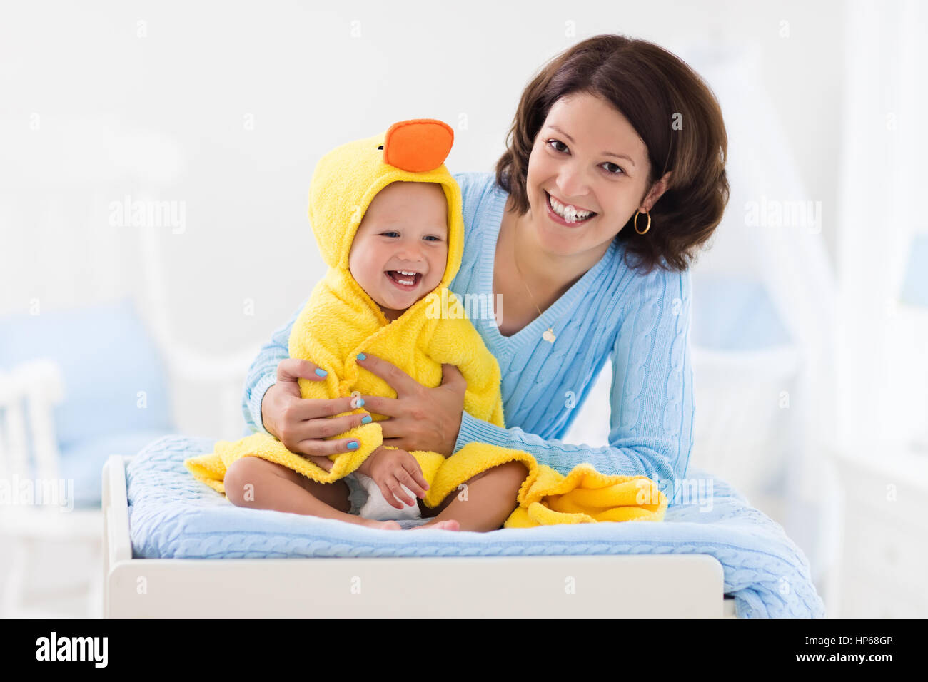 Mother and baby change diaper after bath in white nursery. Little boy
