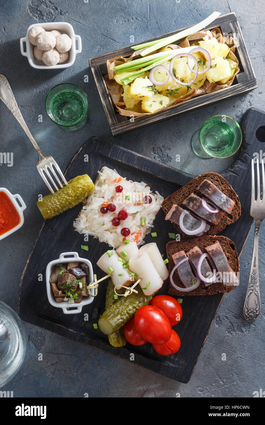 Appetizer food, herring and rye bread on wooden board with vodka and pickles. Stock Photo