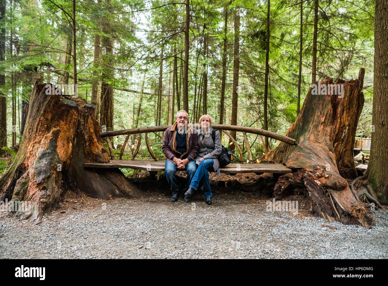 Couple sitting on hand made bench seat made from two old trees at Capilano Suspension Bridge Park Stock Photo