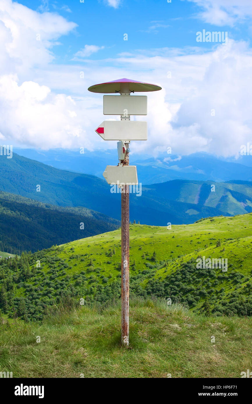 Signpost on the background of mountains and blue sky with clouds. Route post with blank pointer Stock Photo