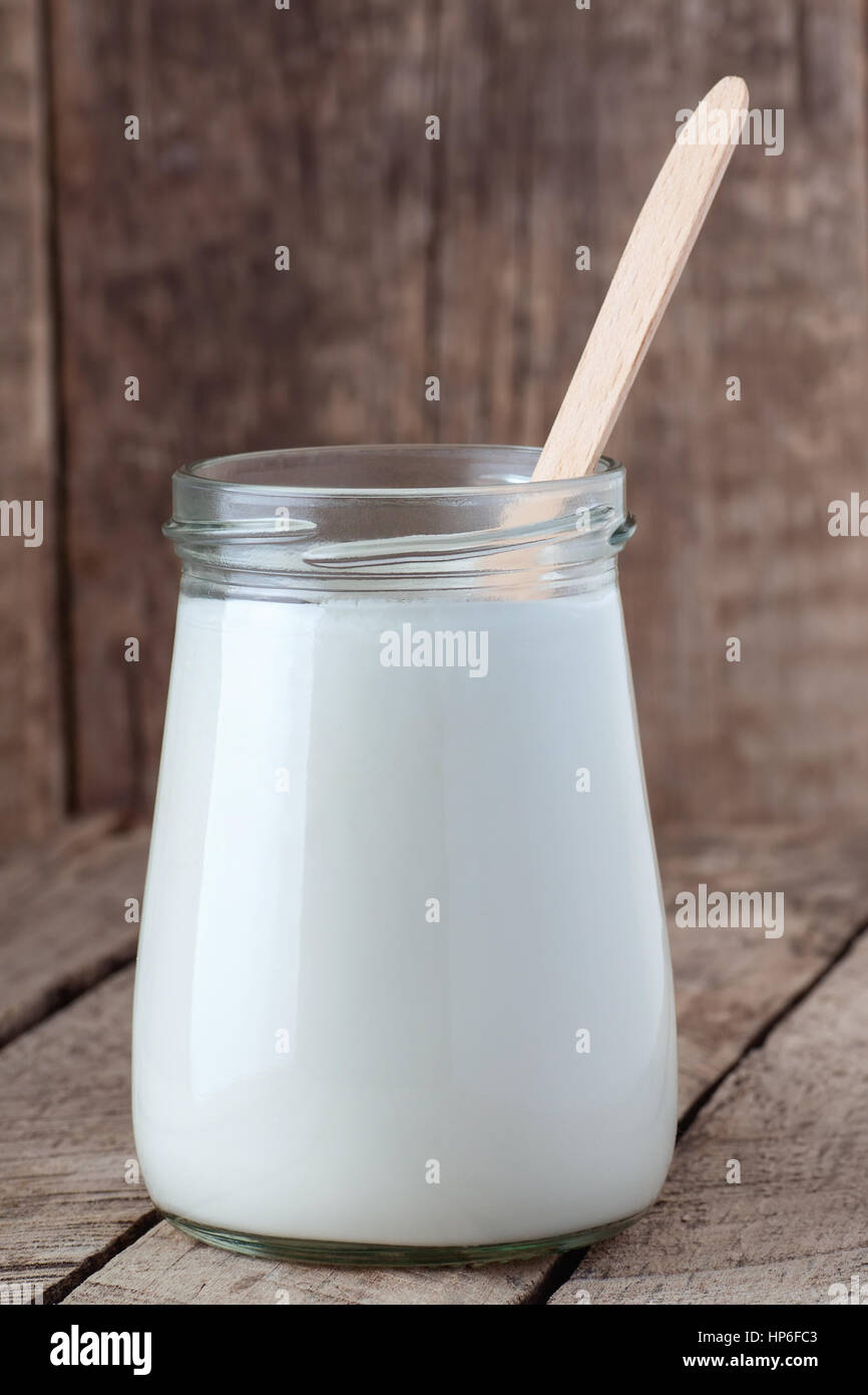 Greek yogurt in a glass jar with spoon on wooden background. Healthy dairy food sour cream on wooden table Stock Photo