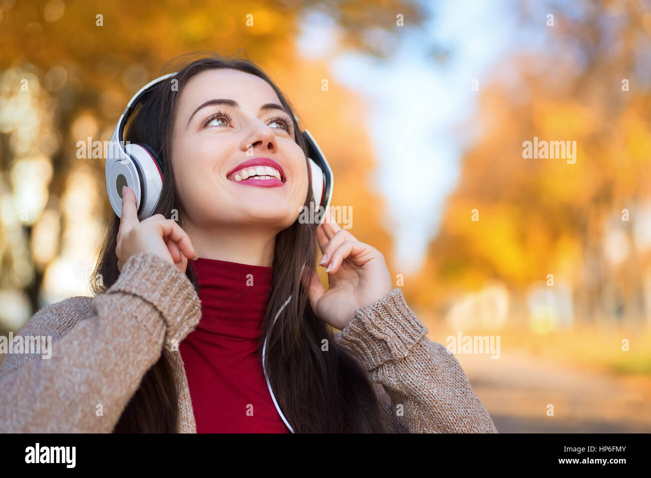 Young happy smiling brunette woman with headphones outdoors on autumn day. Girl listening music in headphones in autumn park. Portrait of woman at out Stock Photo