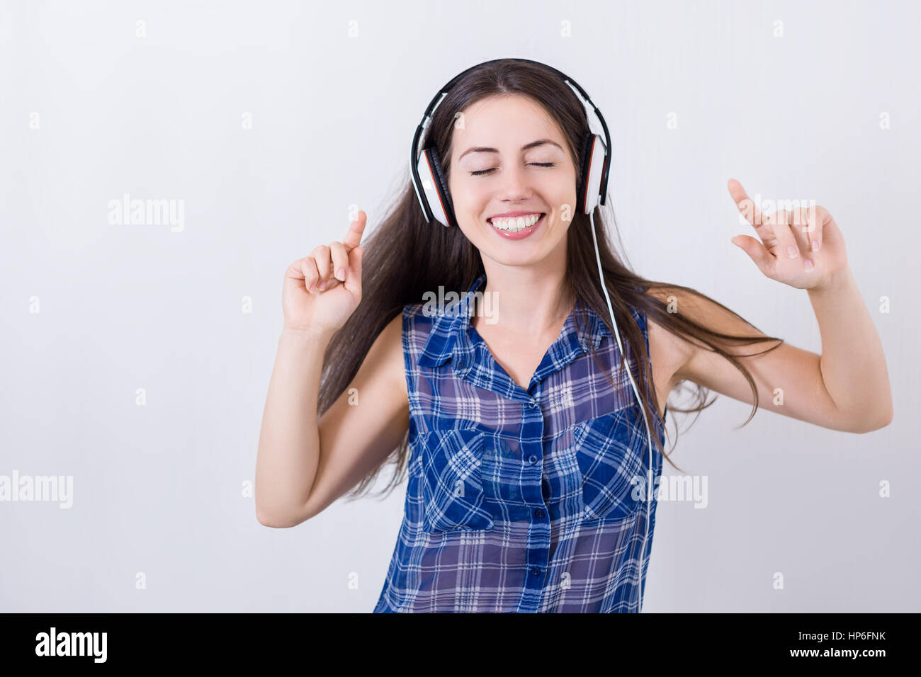portrait of girl listening music wearing headphones with white wall background. Cheerful young woman listening music with headphones and dance with cl Stock Photo