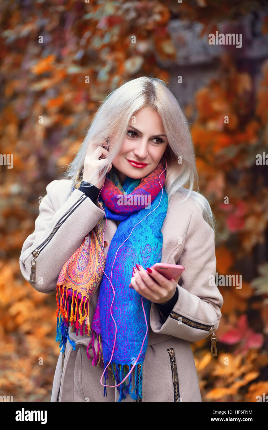 Young beautiful girl listening to MP3 player in autumn park. Beautiful autumn woman listening to music in autumn park enjoy autumn day.Beautiful young Stock Photo