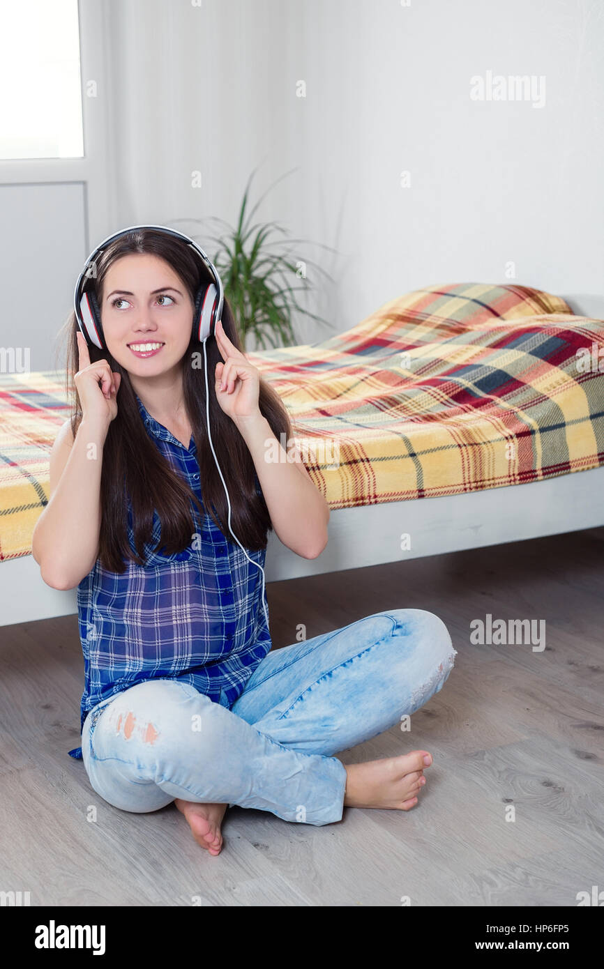people, leisure and technology concept - happy woman or teenage girl in headphones listening to music at bedroom. Girl listening to music. Young smili Stock Photo
