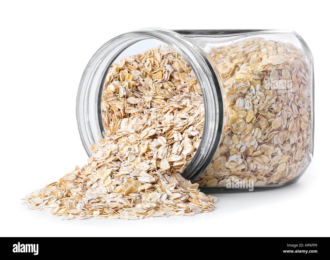 transparent glass jar with rolled oats isolated on white background. Glass jar with oatmeal flakes lying on side isolated on white background. Scatter Stock Photo