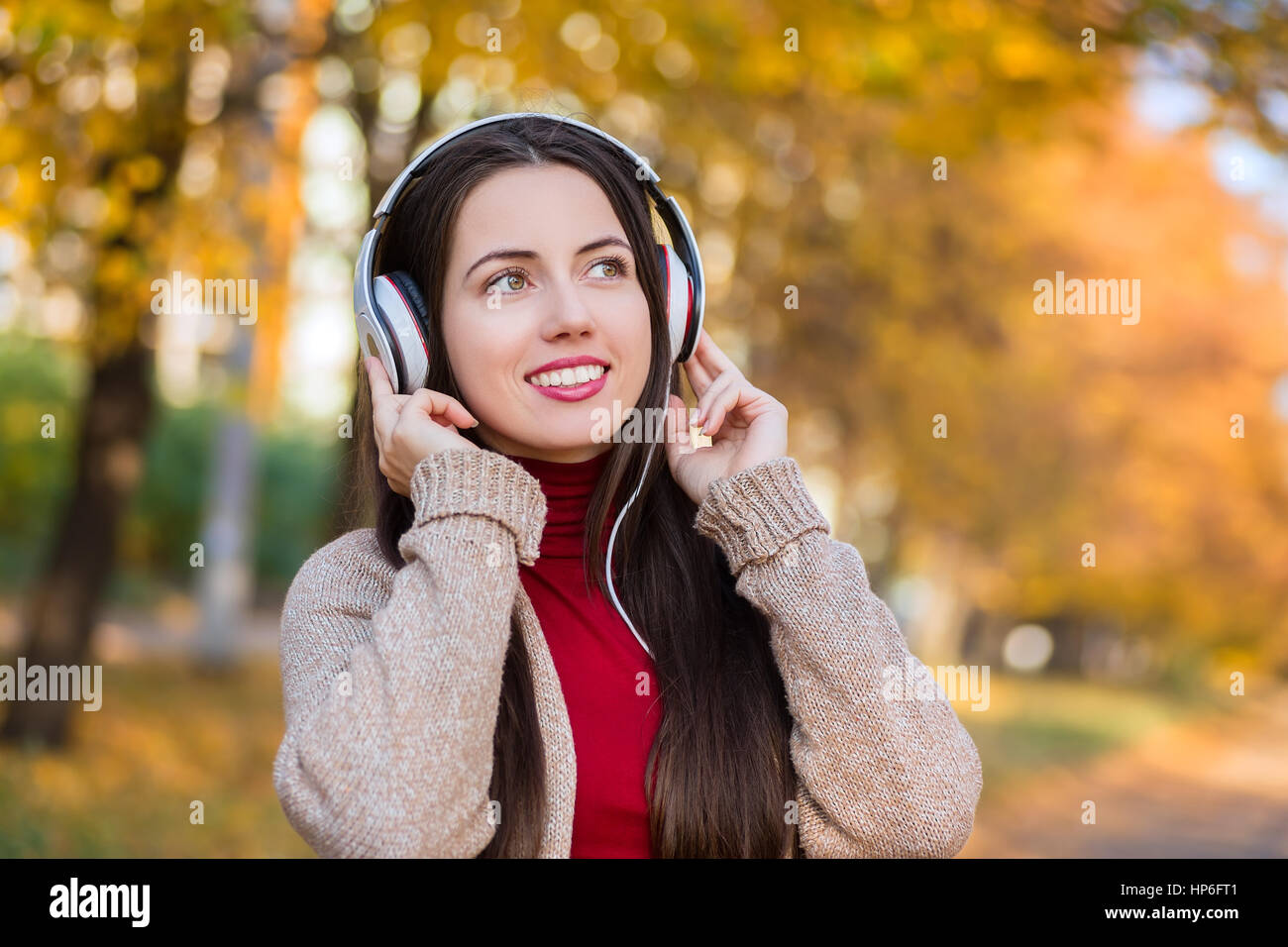 Young caucasian brunette woman with headphones outdoors on autumn day. Girl listening music in headphones in autumn park. Portrait of woman at outdoor Stock Photo