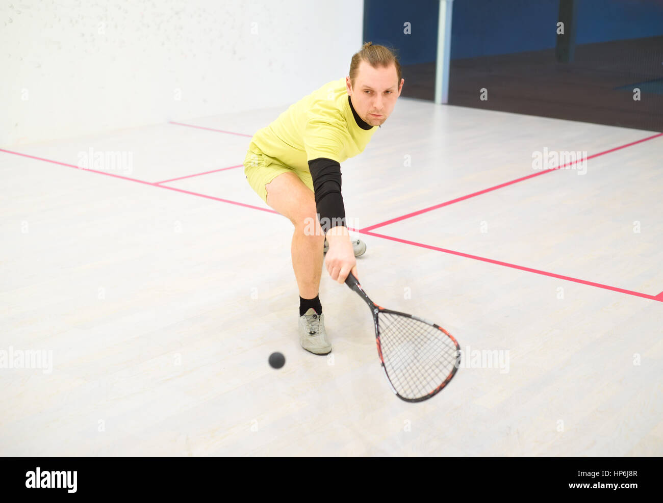 young caucasian squash player hitting a ball in a squash court. Squash player in action. Man playing match of squash Stock Photo