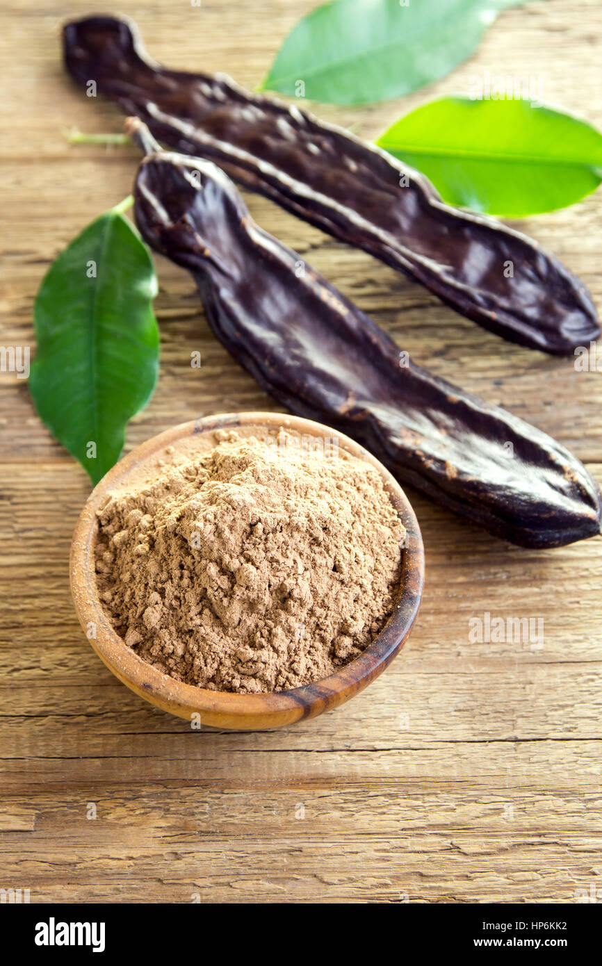 Carob pods and carob powder over wooden background with copy space organic healthy ingredient