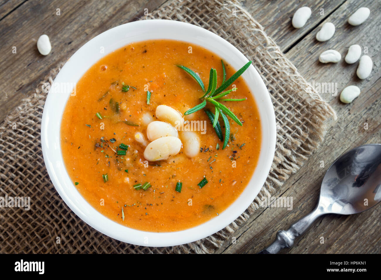 Creamy white bean and vegetable soup with rosemary on wooden background