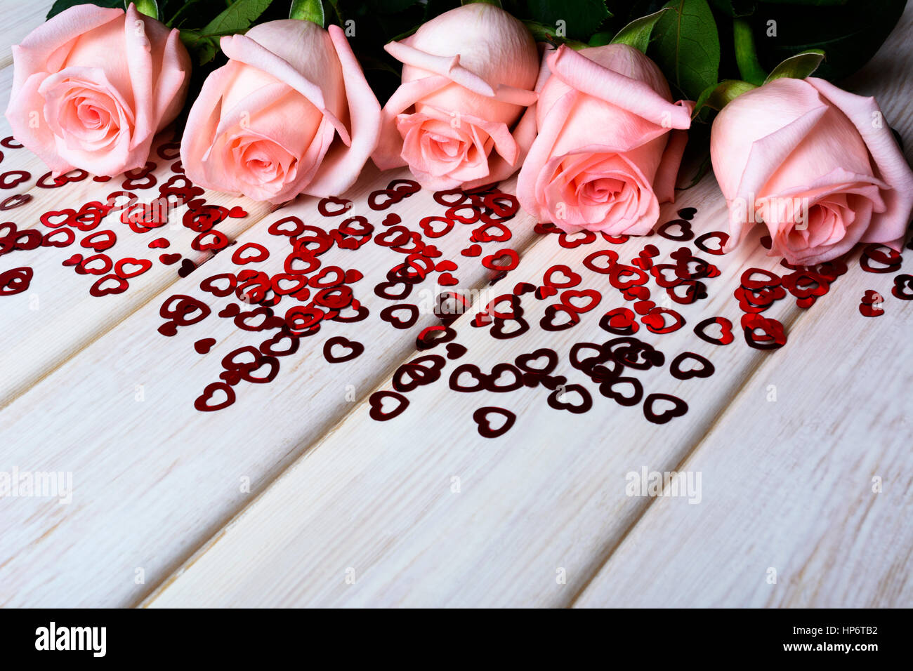 Fall in love concept with pale pink roses and small red hearts. Elegant wedding invitation. St. Valentine greeting card background. Copy space. Stock Photo