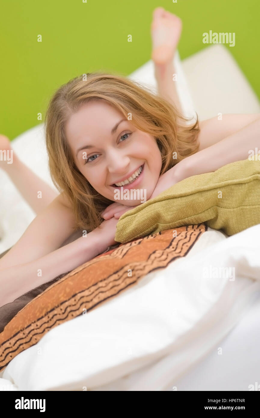 Model released , Junge Frau, 25+, liegt mit Kissen auf dem Bett - woman with pillows lying on the bed Stock Photo