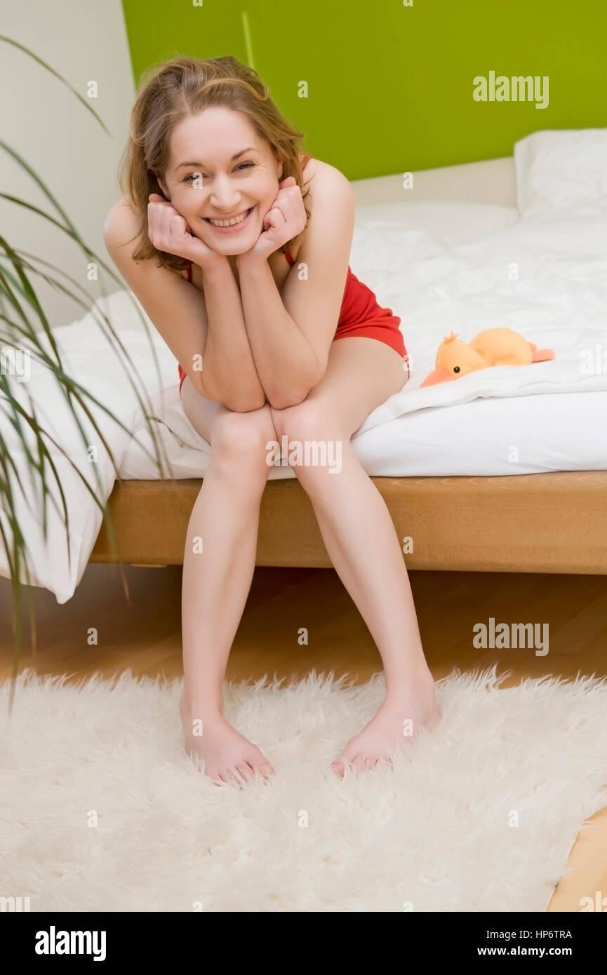 Model released , Junge, attraktive Frau, 25+, sitzt lachend auf Bettkante - young, laughing woman in bedroom sitting on bed Stock Photo