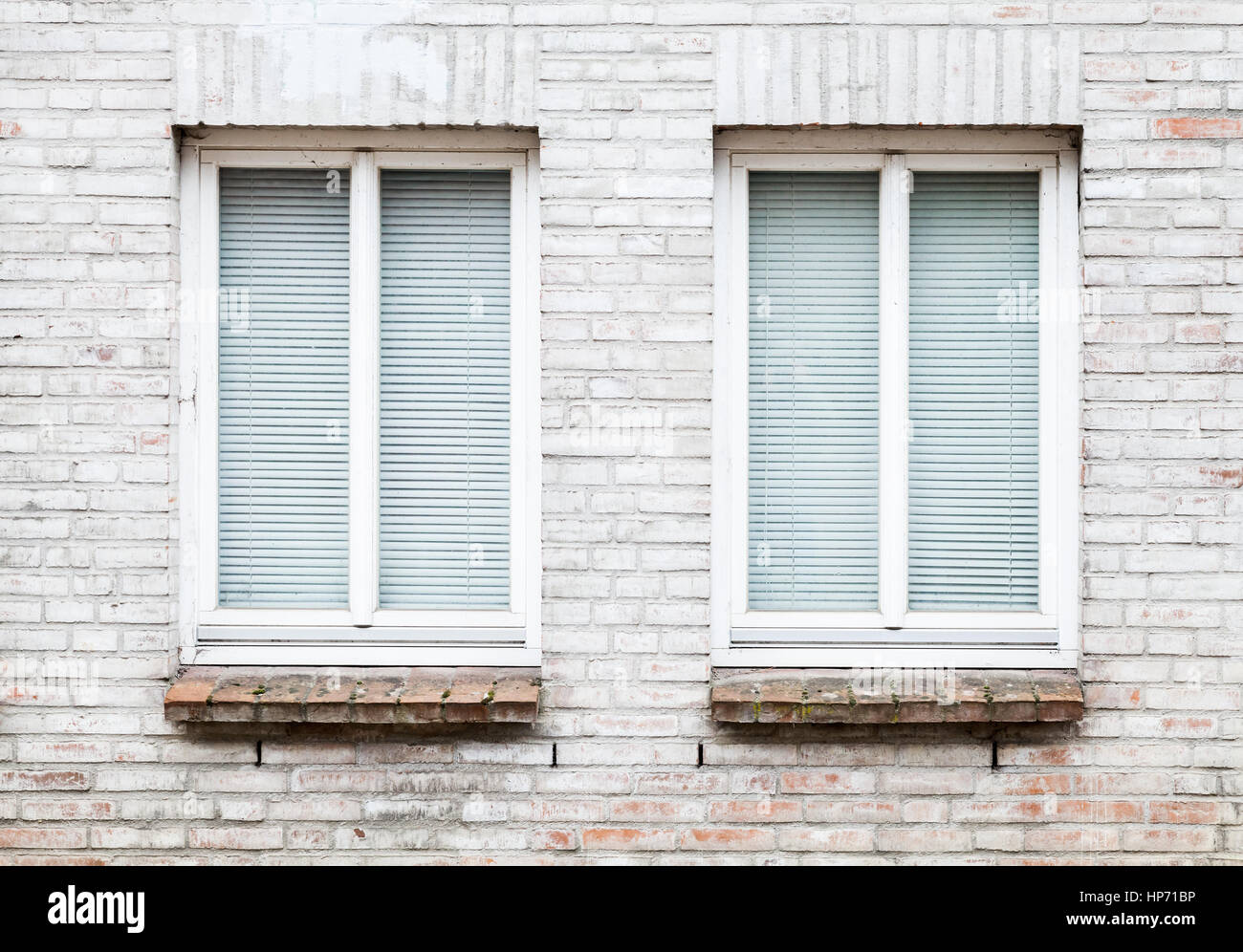 Gray brick wall with two windows closed with white louvers, background texture Stock Photo