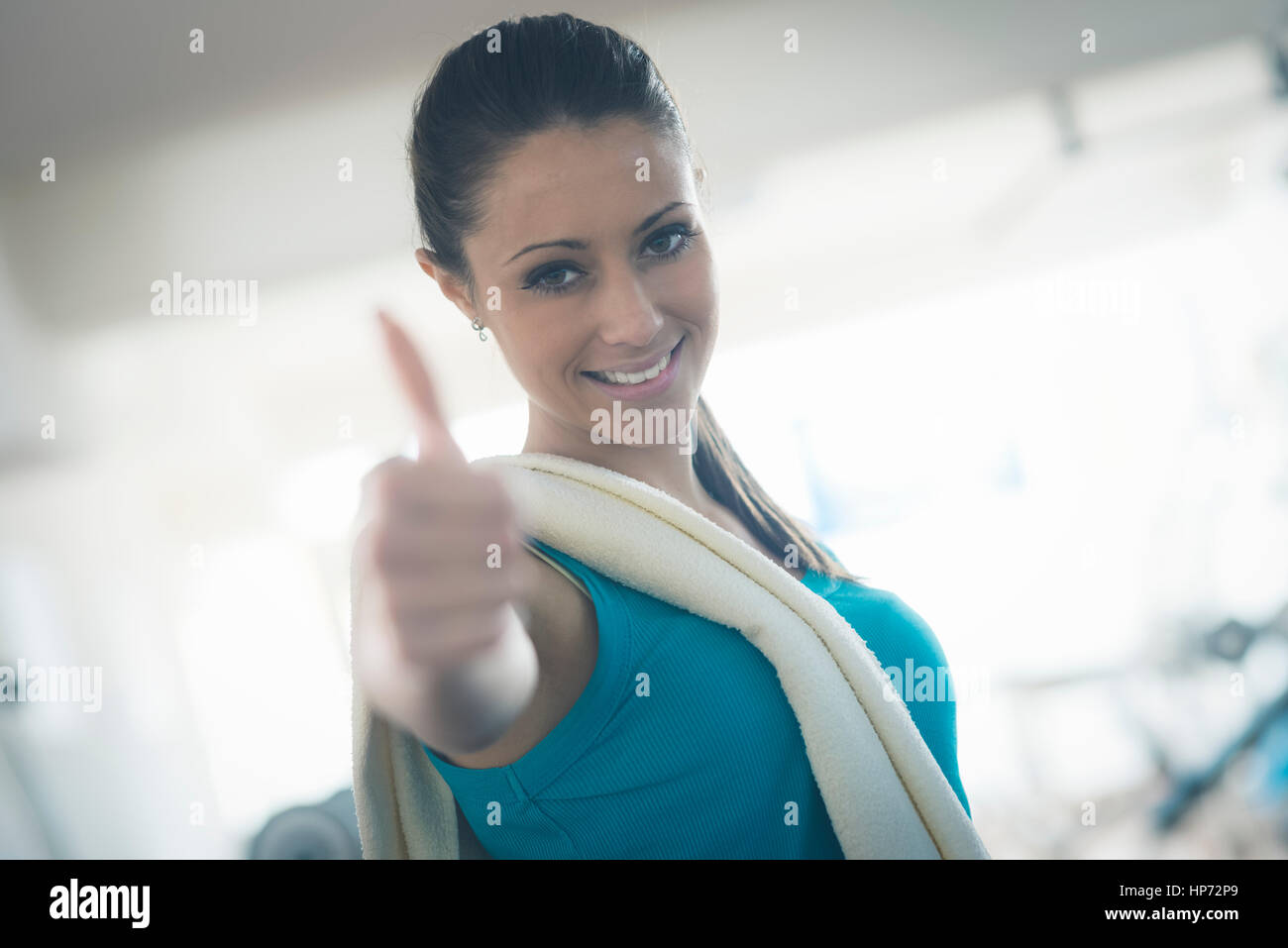 Attractive young woman with towel at gym smiling at camera thumbs up ...