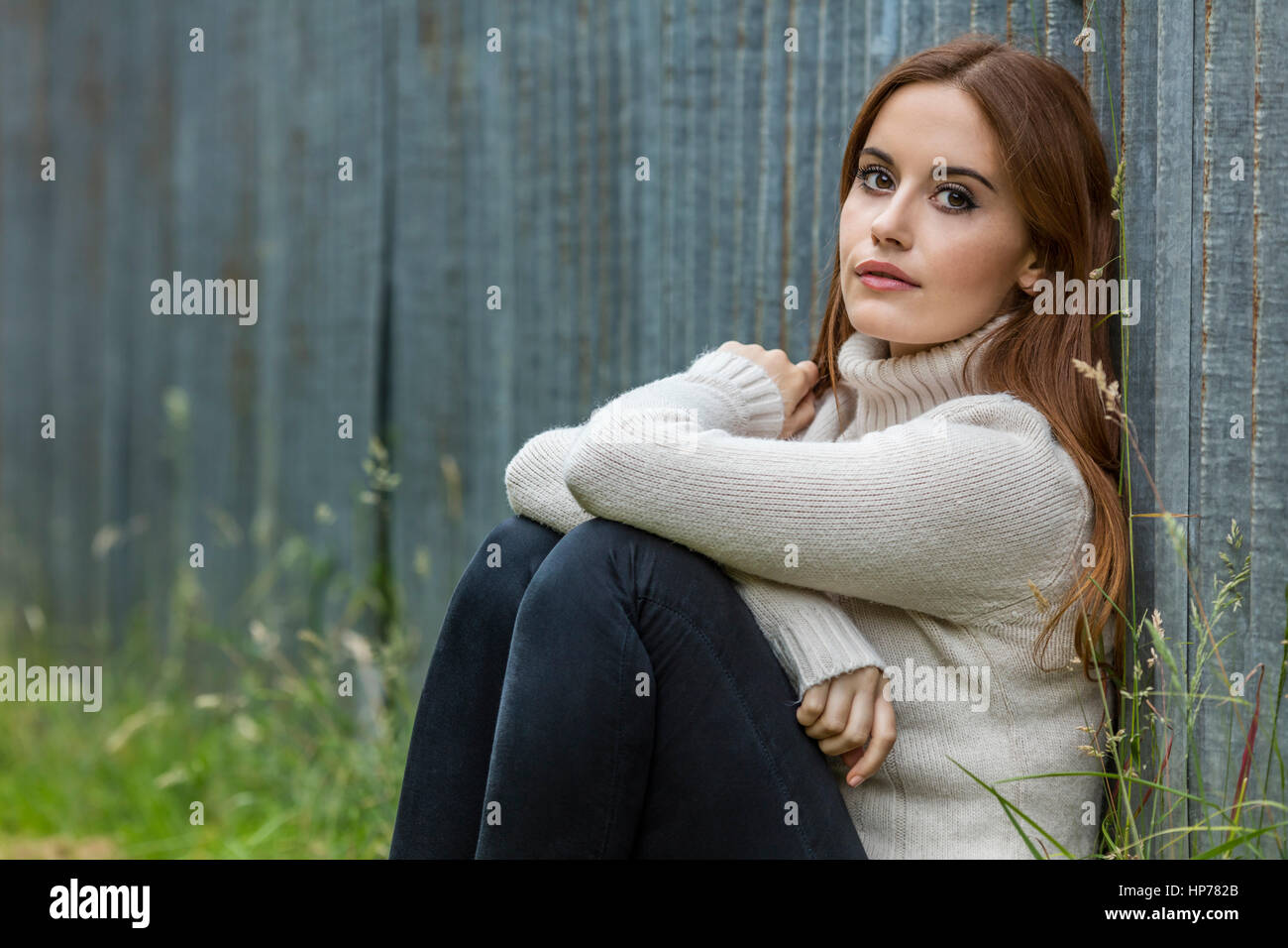 Outdoor portrait of beautiful thoughtful girl or young woman with red hair wearing a white jumper Stock Photo