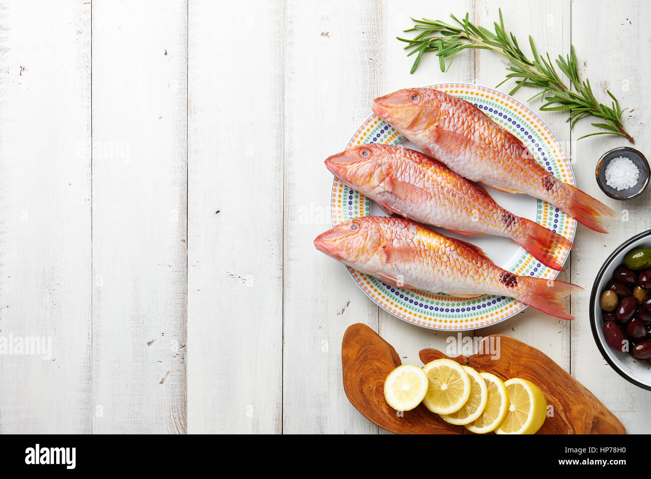 Fresh red mullet fish cooking with oil, herbs and lemon on white wooden