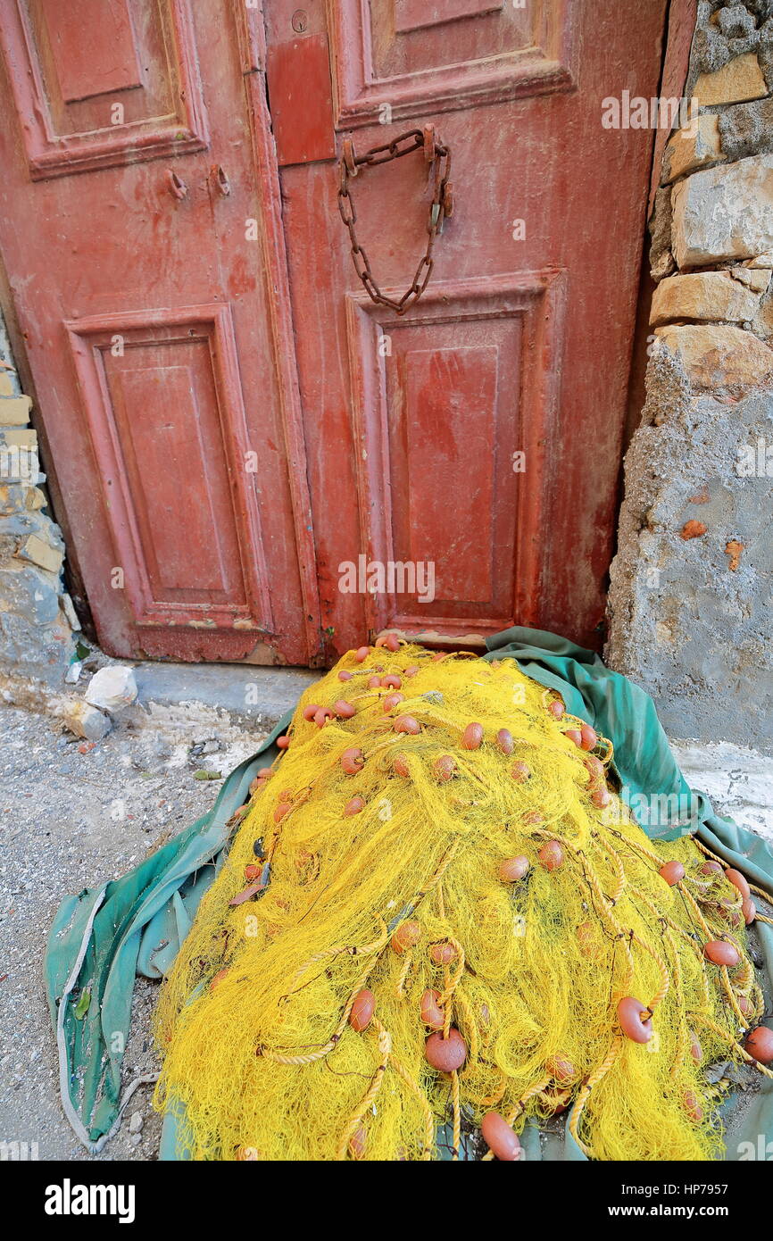Yellow fishing net left to dry on green cloth on the floor of backstreet in the central harbor area facing a maroon painted old door with rusty chain  Stock Photo