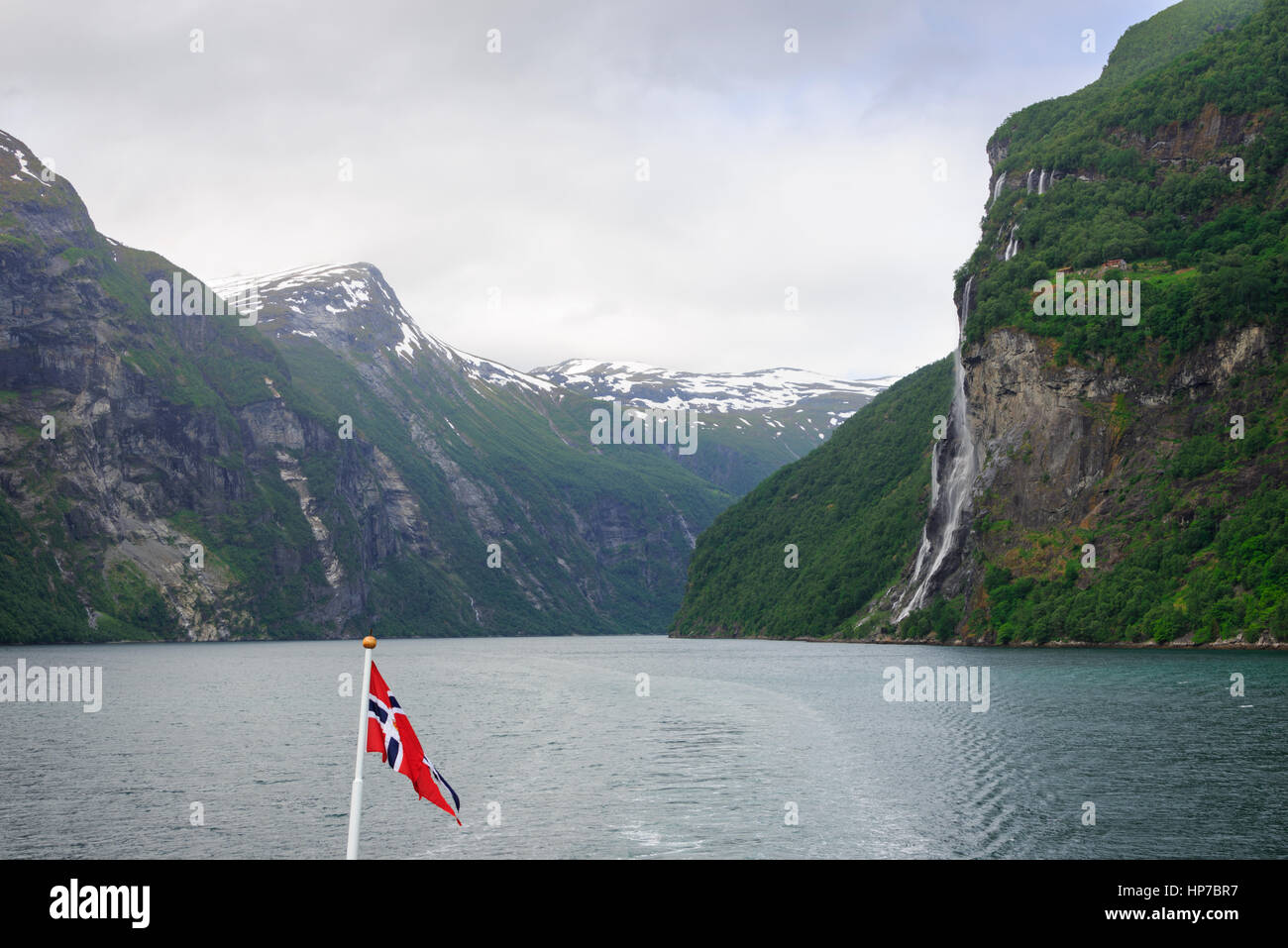 Seven Sisters waterfall falling of the mountain seen from a car ferry ship with a Norwegian flag on the Geirangerfjord to Geiranger, Norway. Stock Photo