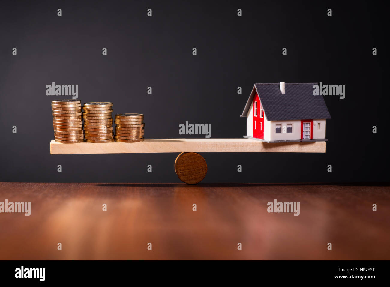 Seesaw with a house on one side and stacks of coins on the other side. Stock Photo
