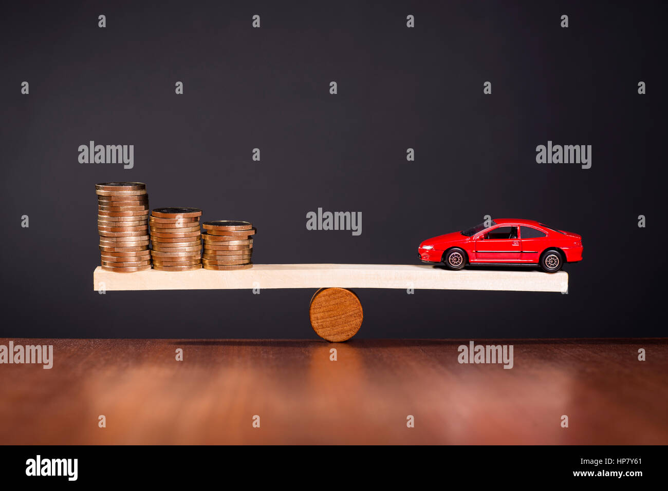 Seesaw with a car on one side and stack of money on the other side. Stock Photo