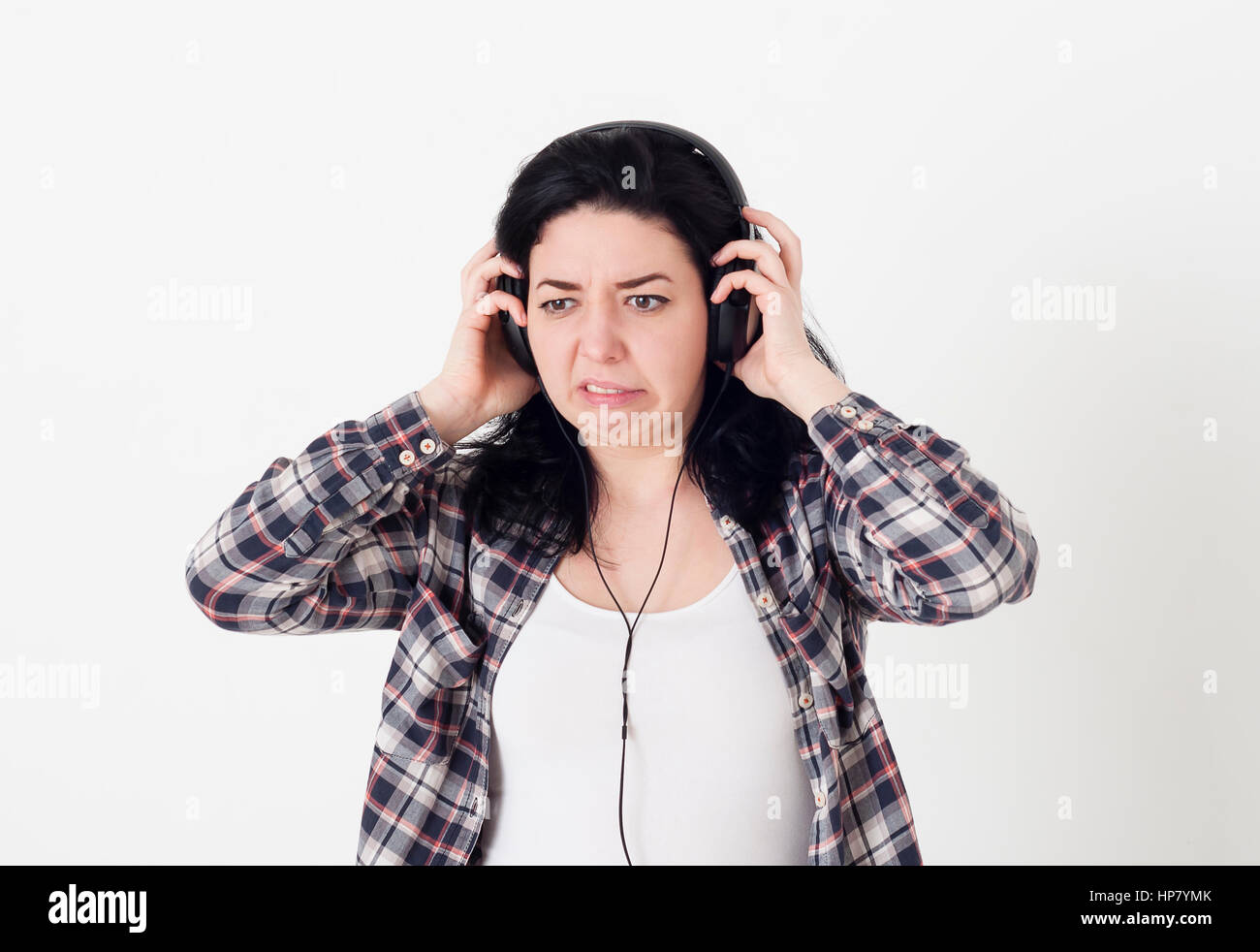Woman heard a very bad music or unpleasant noise in the headphones, she twisted face and wants to remove the headphones from the head. Stock Photo