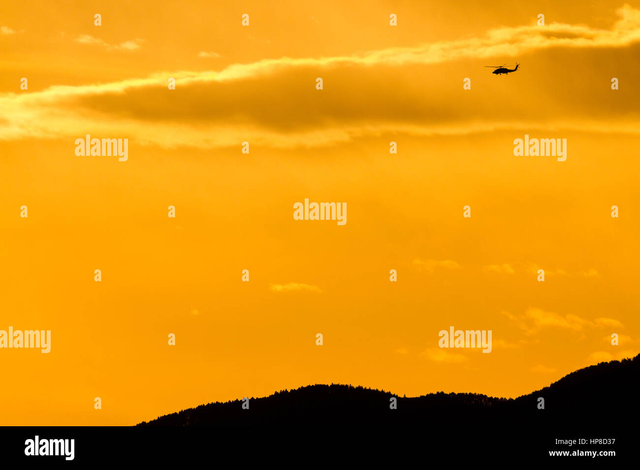 A silhouetted US Navy SH60 Seahawk helicopter flying in sunset light over mountains in Kanagawa, Japan. Stock Photo