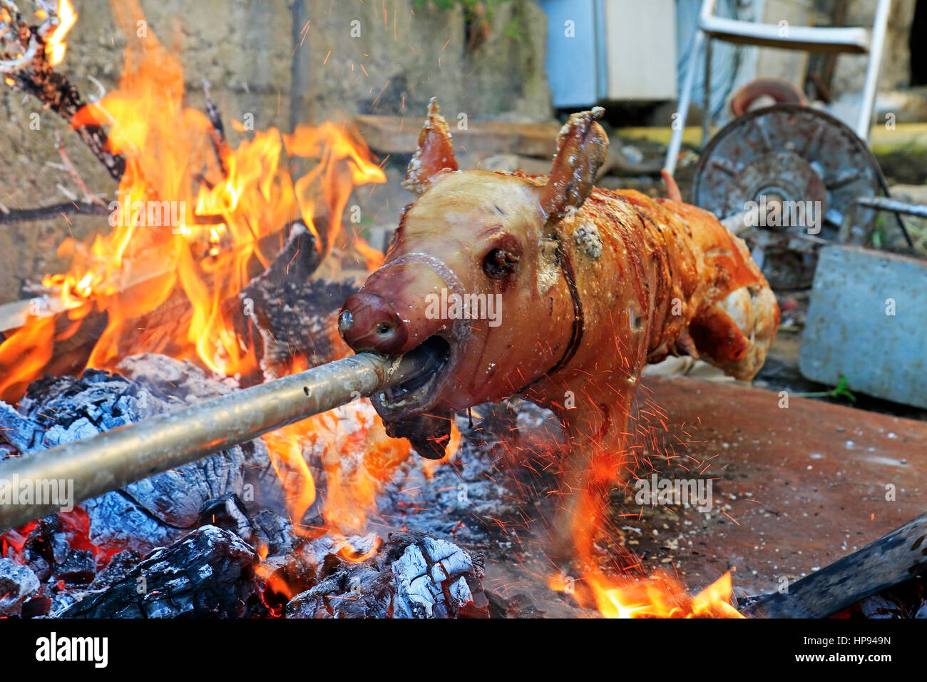 Suckling pig on a rotating spit with fire and sparks around Stock Photo