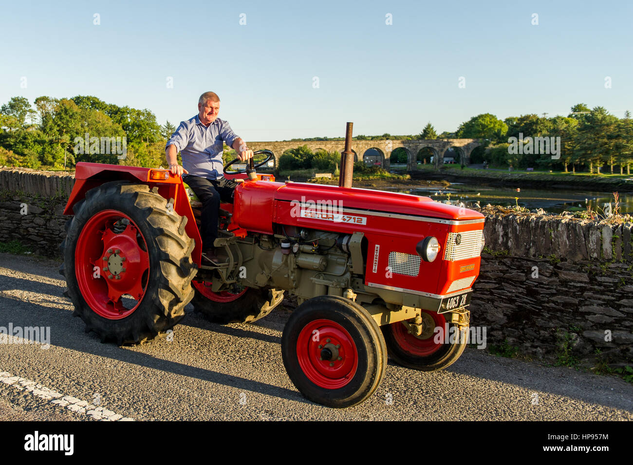 Zetor 4712 tractor crosses a bridge in Ballydehob, West Cork, Ireland with the famous 12 Arch Bridge in the background with copy space. Stock Photo