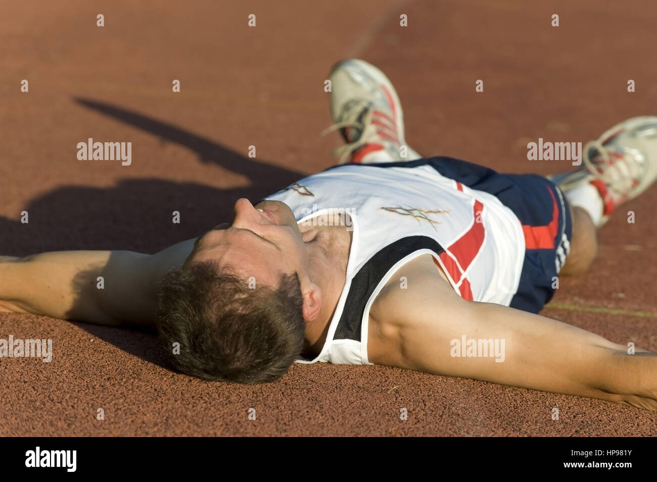 Model released , Sportler liegt erschoepft auf der Laufbahn - exhausted sportsman lying on ground Stock Photo