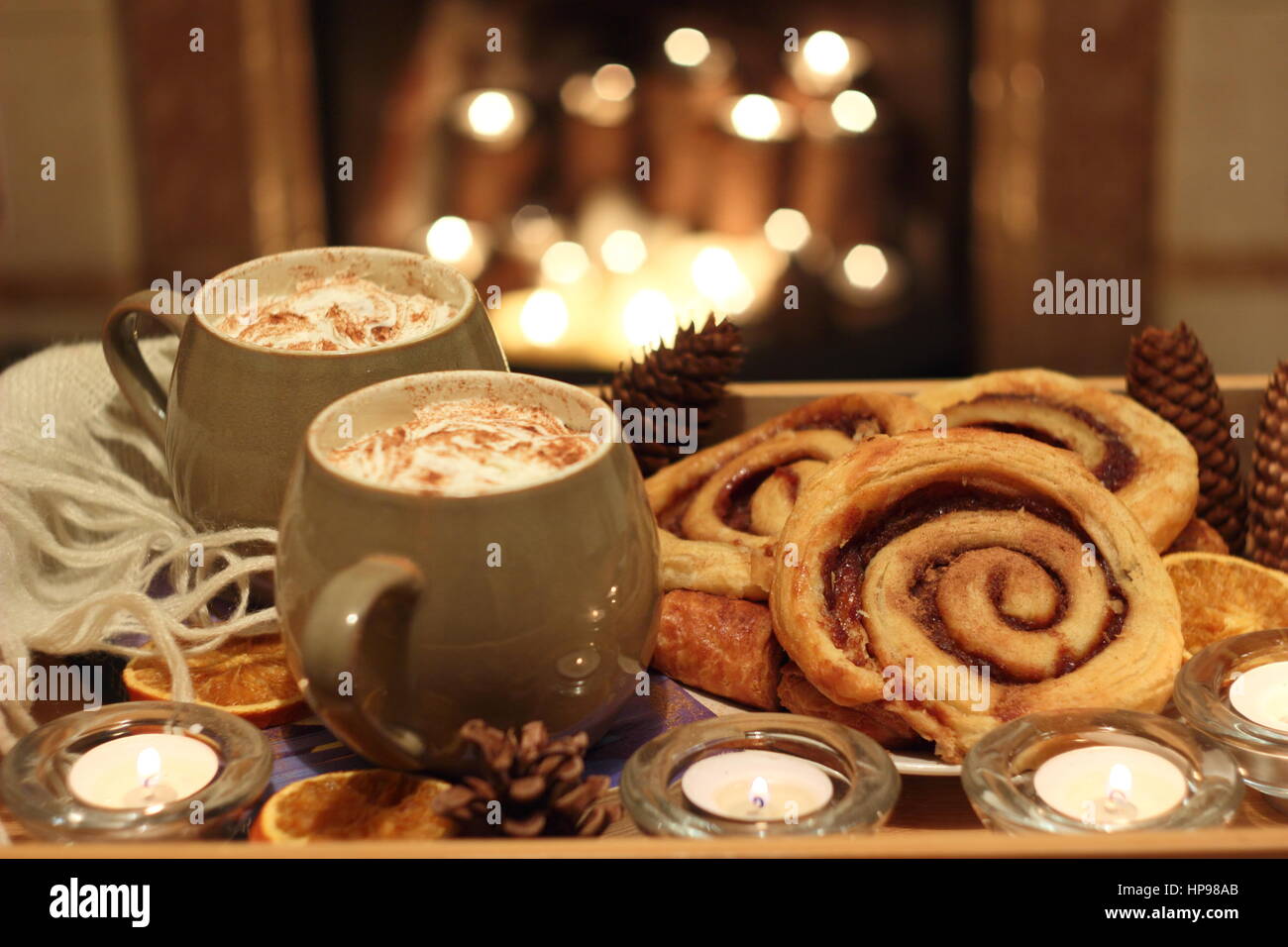 Creamy mugs of mocha - coffee and chocolate - are served with cinnamon buns by a candle lit open fireplace in a cosy English home Stock Photo