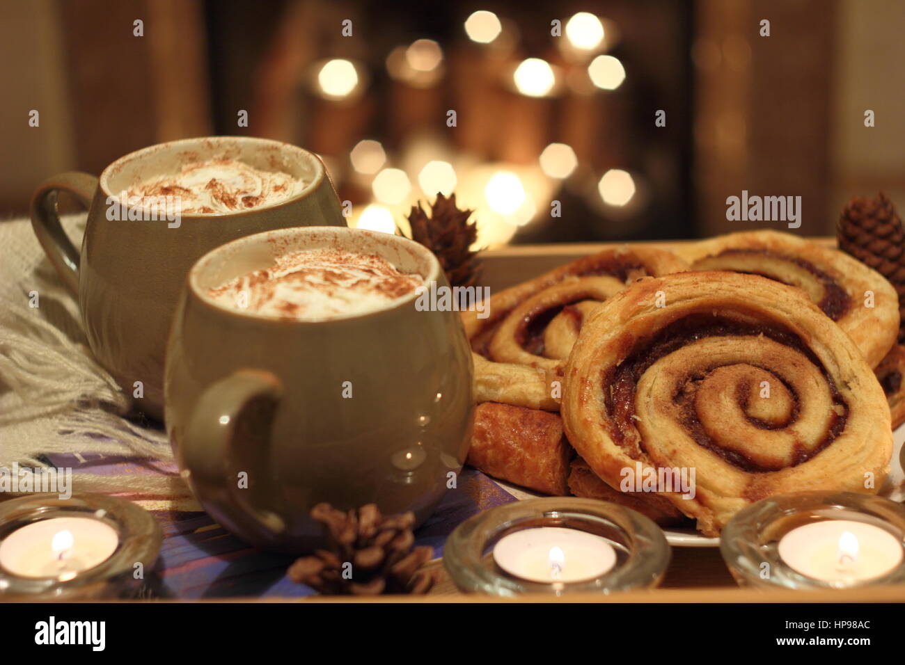 Creamy mugs of mocha - coffee and chocolate - are served with cinnamon buns by a candle lit open fireplace in a cosy English home Stock Photo